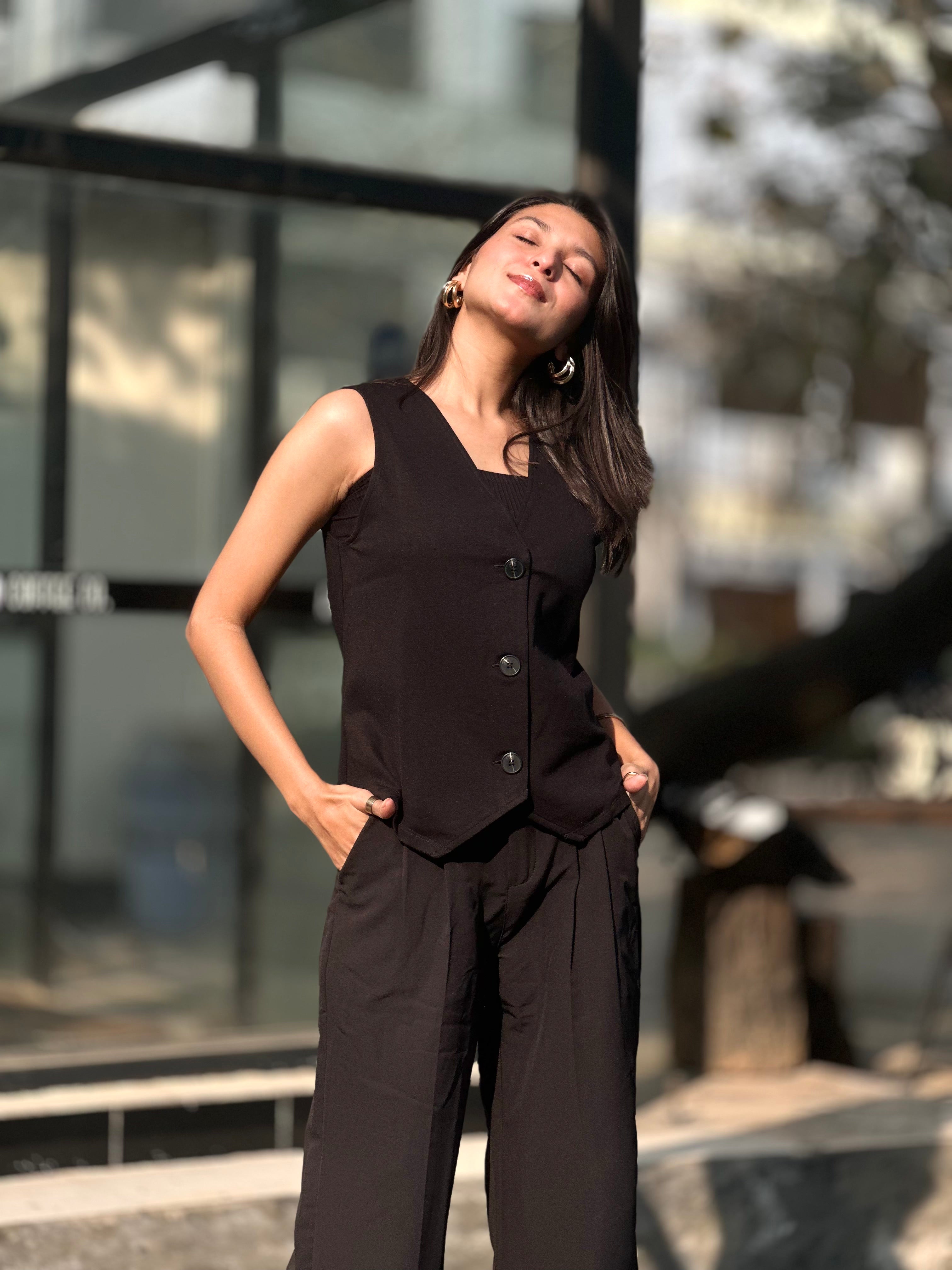 Woman in a black sleeveless top and pants standing outdoors with a blurred background