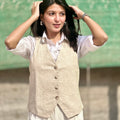 Woman wearing a beige vest over a white shirt with a green background