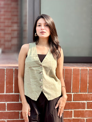 Woman wearing a light green vest over a black top against a brick wall.