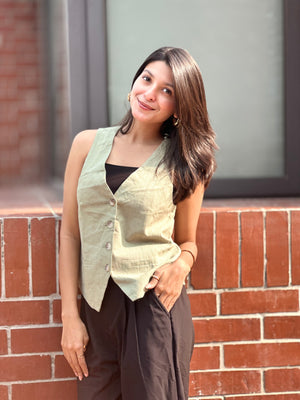 Woman standing against a brick wall wearing a light green vest over a black top.