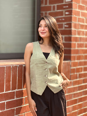 Woman wearing a light green vest standing against a brick wall.