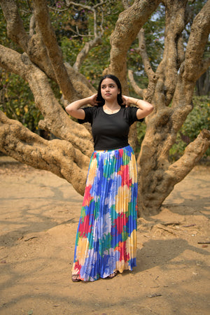 Person with a colorful skirt standing on a sandy beach with large trees in the background. trendybuzz