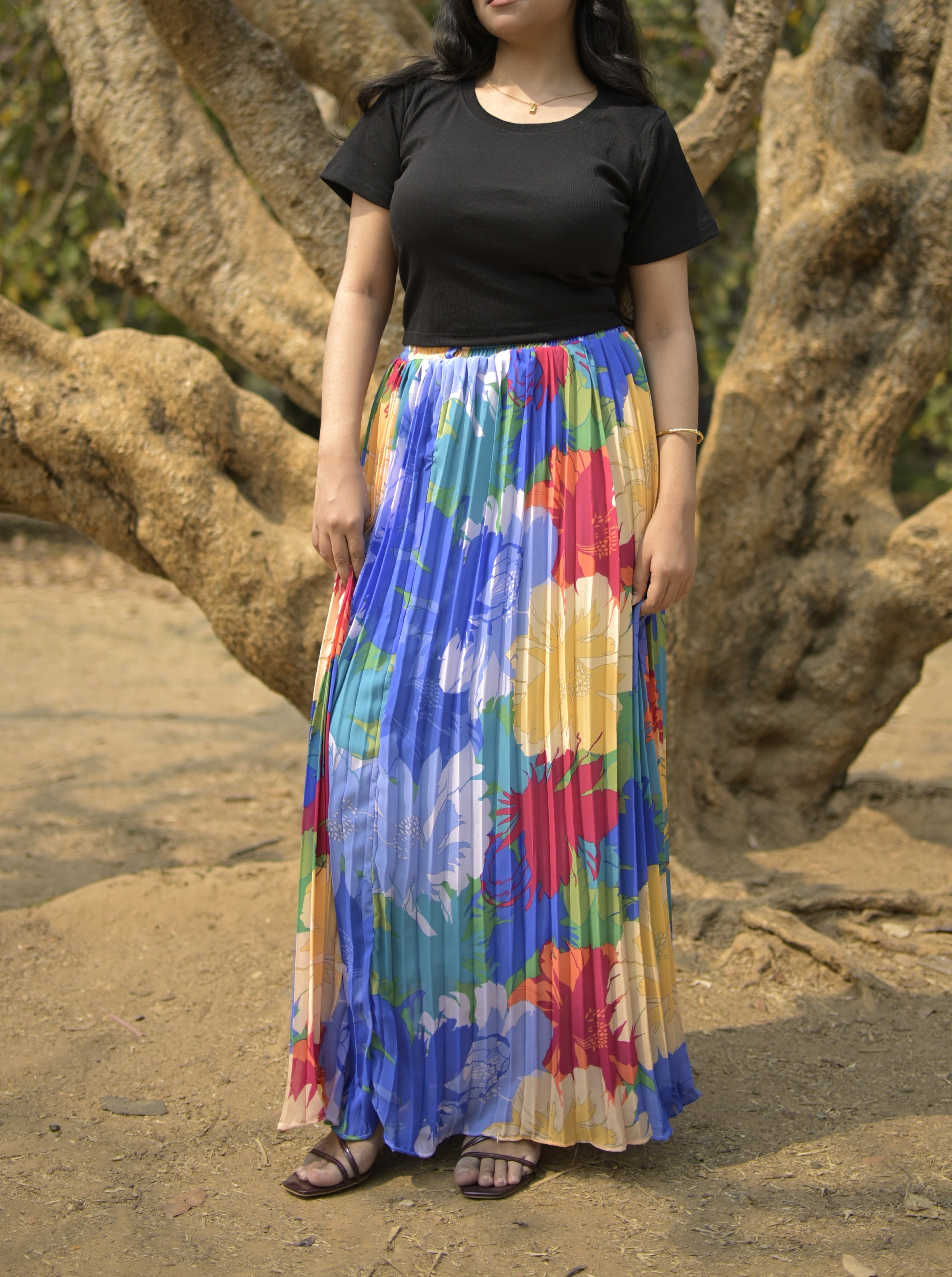Person wearing a black top and colorful skirt standing in front of a tree trendybuzz