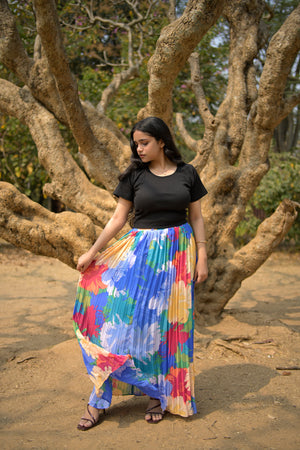 Person wearing a colorful dress standing on a sandy beach with large tree trunks in the background trendybuzz