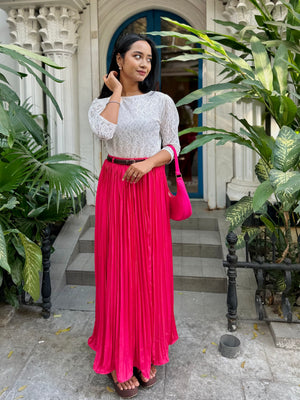 Woman in a white top and pink skirt standing in front of a building with plants.