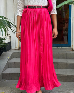 Person wearing a long pink skirt with a white top and black belt, standing on a concrete step.