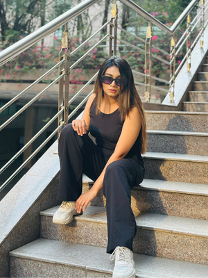 A person wearing a sleeveless tan crop top and black pants, seated on outdoor stairs.