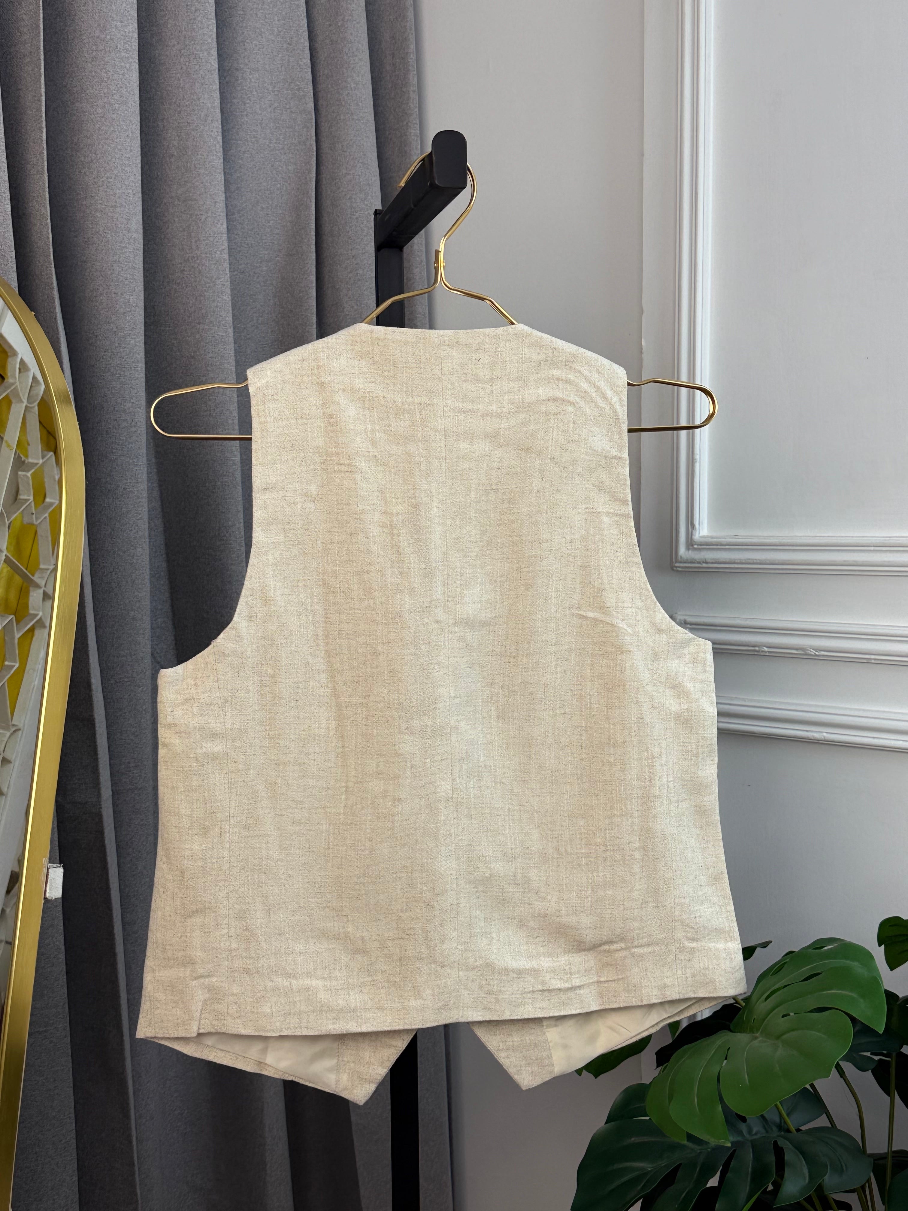Beige sleeveless top on a hanger against a gray curtain background