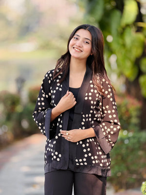 Woman wearing a black polka dot jacket outdoors with greenery in the background