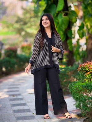 Woman in black outfit with checkered jacket standing on a pathway with greenery