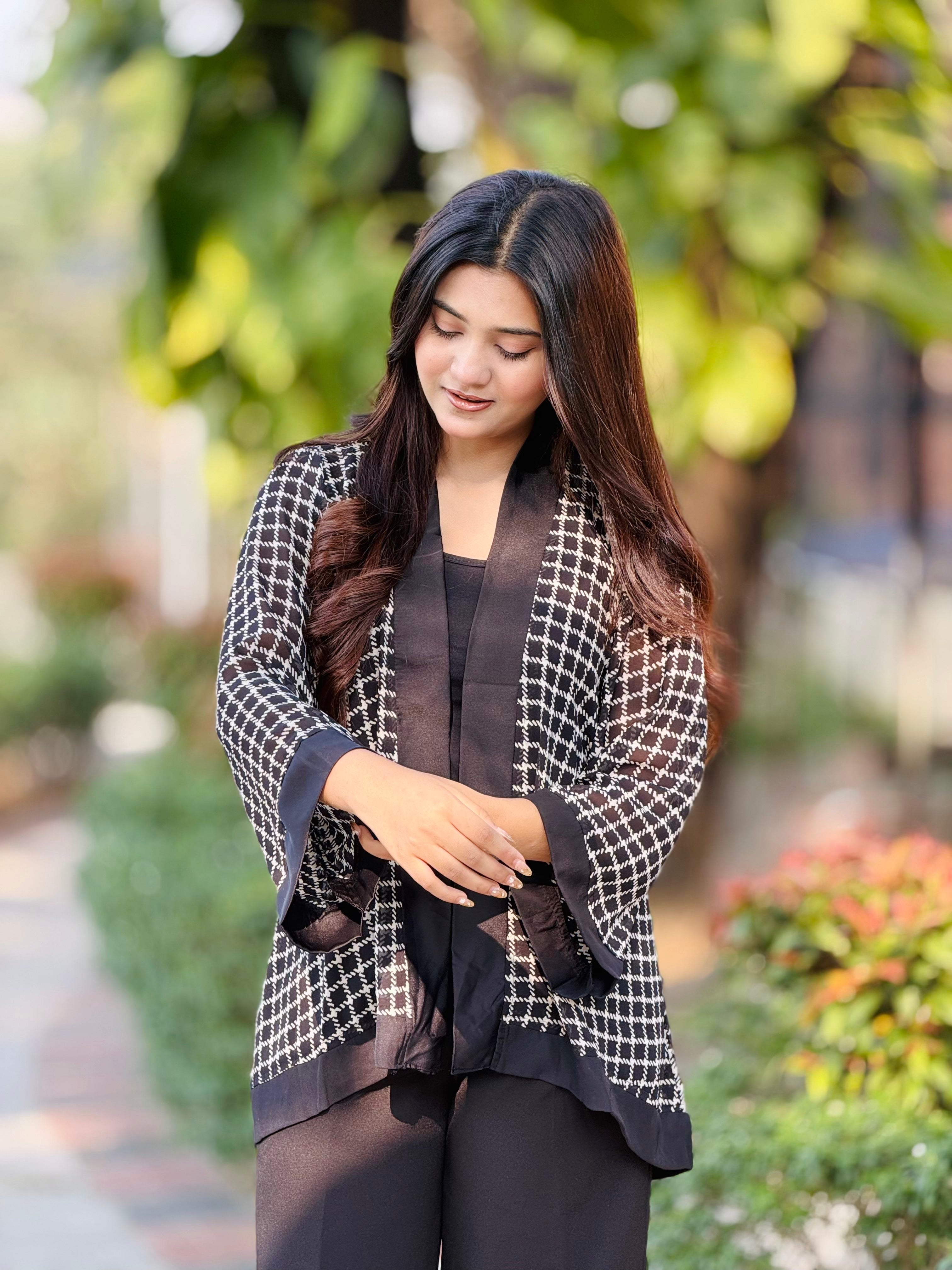 Woman wearing a black and white checkered jacket outdoors with greenery in the background