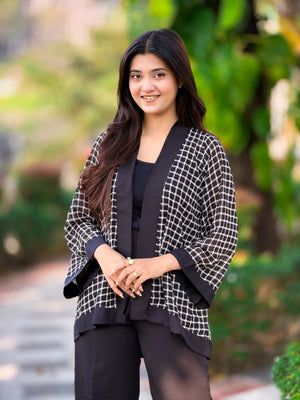Woman wearing a black and white patterned jacket outdoors with greenery in the background