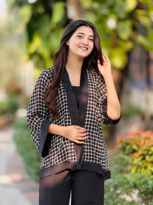 Woman wearing a black and white checkered jacket outdoors with greenery in the background
