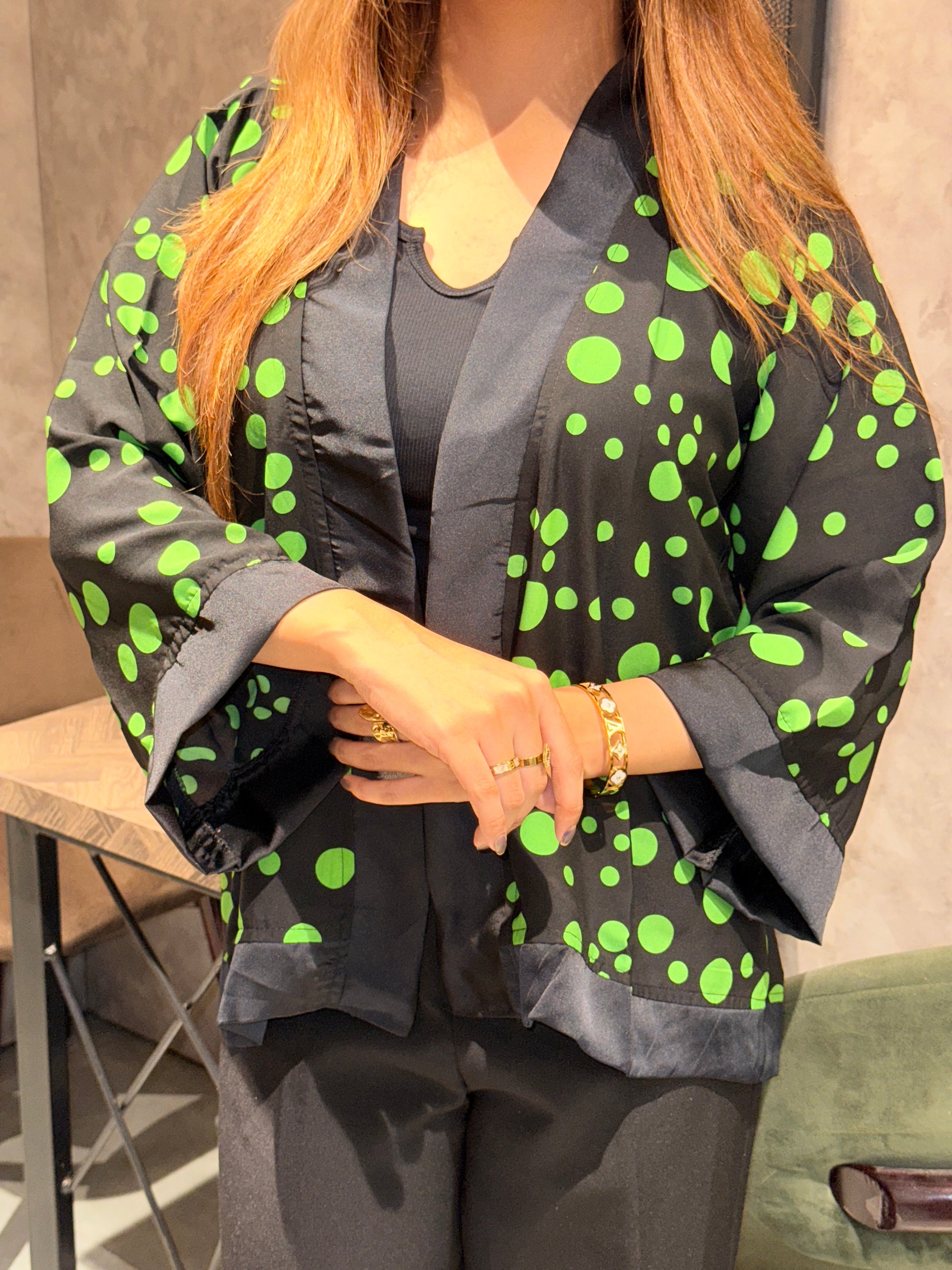 Person wearing a black outfit with green polka dots sitting on a couch.