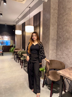 Woman in a black Polka dot Kimono Outfit standing in a modern interior setting with tables and chairs.