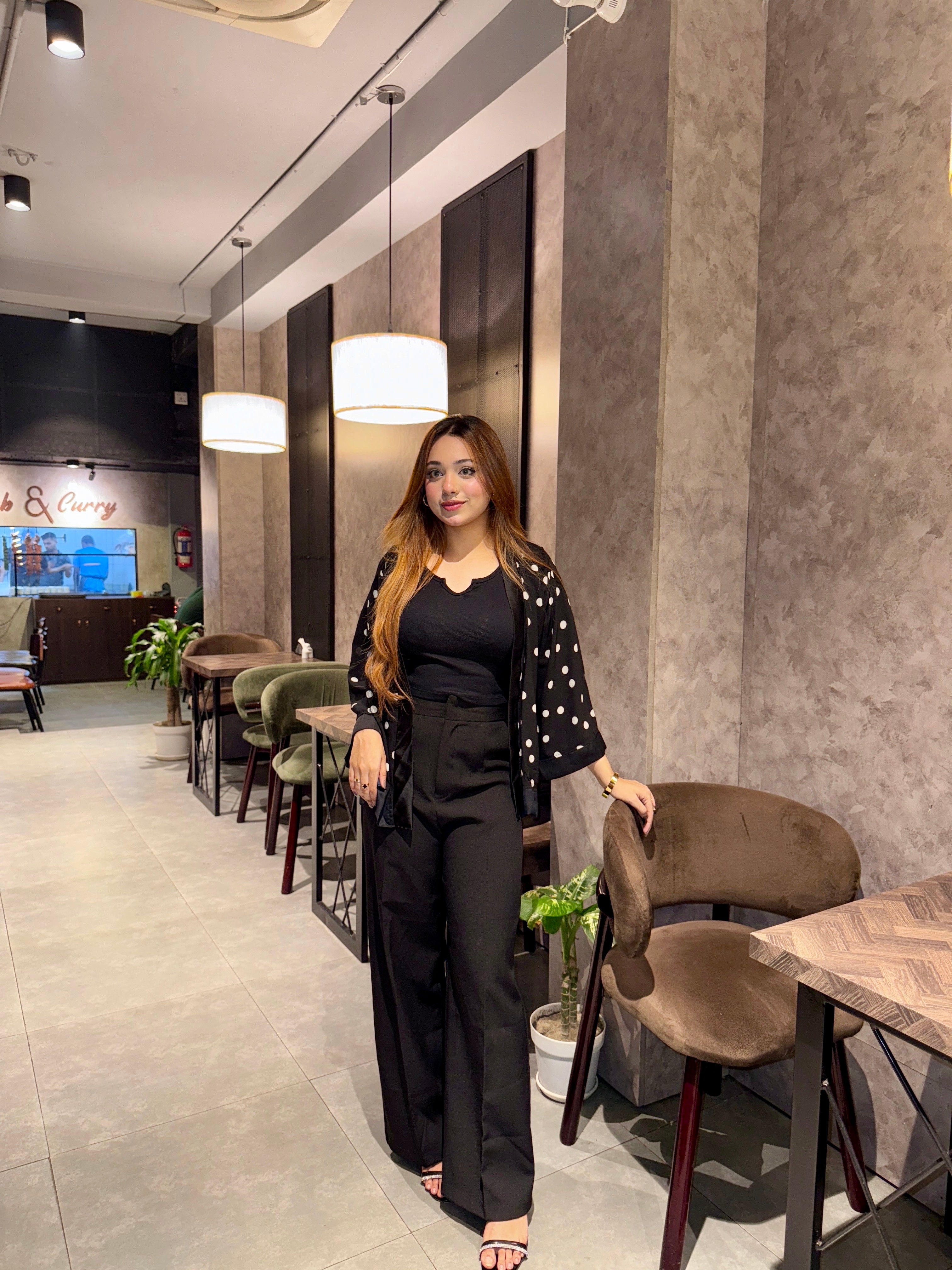 Woman in a black Polka dot Kimono Outfit standing in a modern interior setting with tables and chairs.