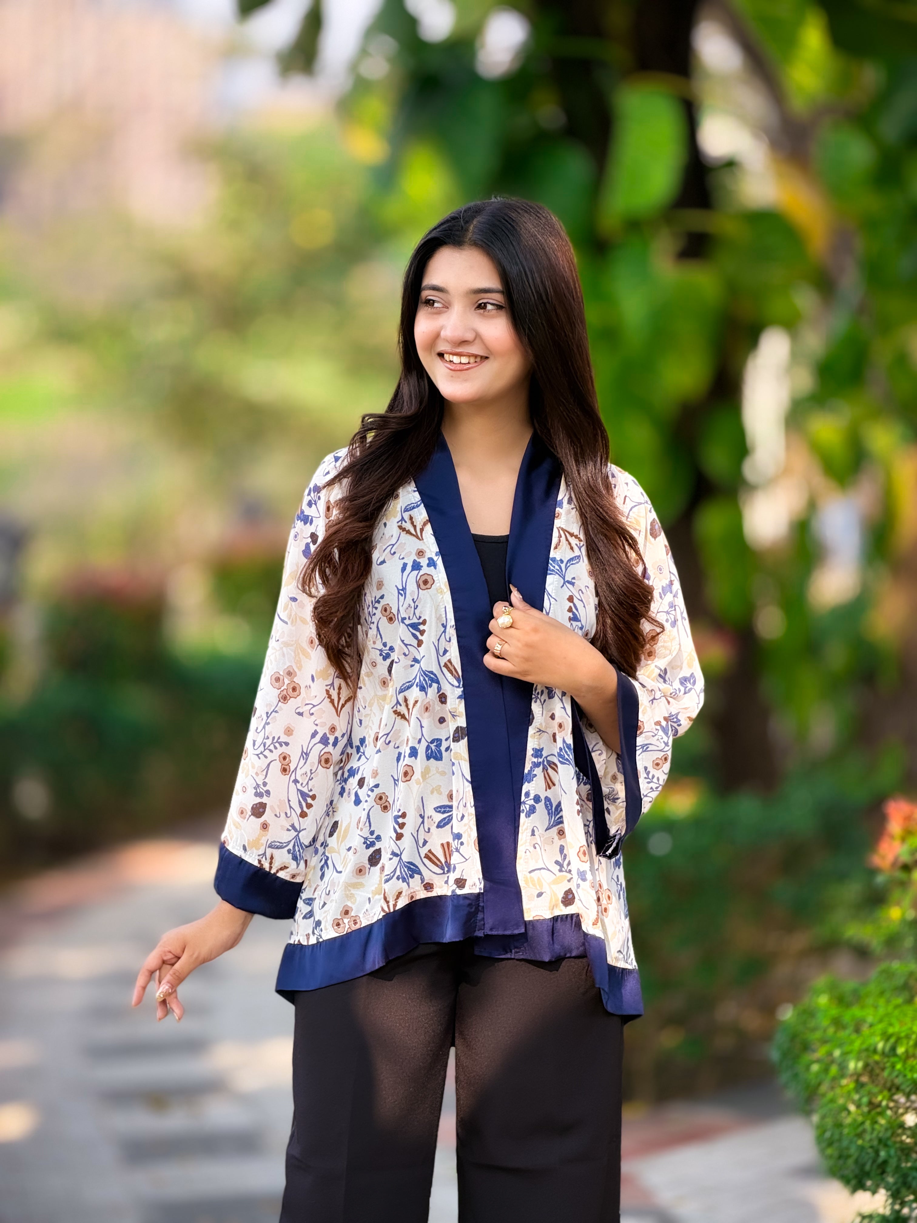 Woman wearing a floral kimono-style top with a blurred green outdoor background
