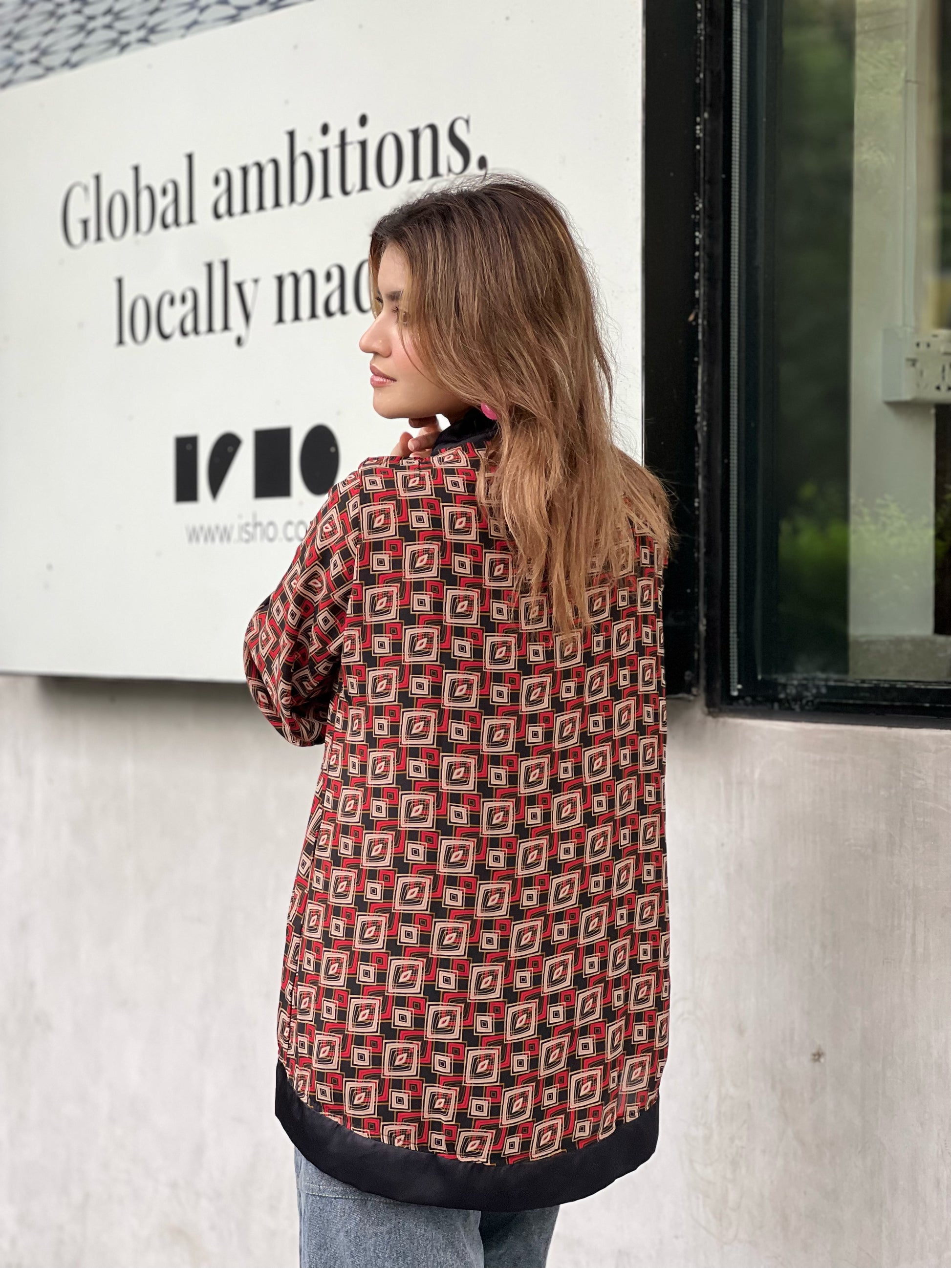 Woman wearing a patterned short kimonos standing in front of a building with a sign.