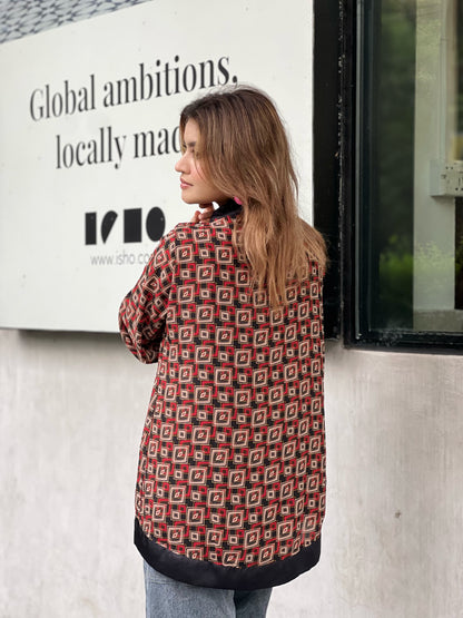 Woman wearing a patterned short kimonos standing in front of a building with a sign.