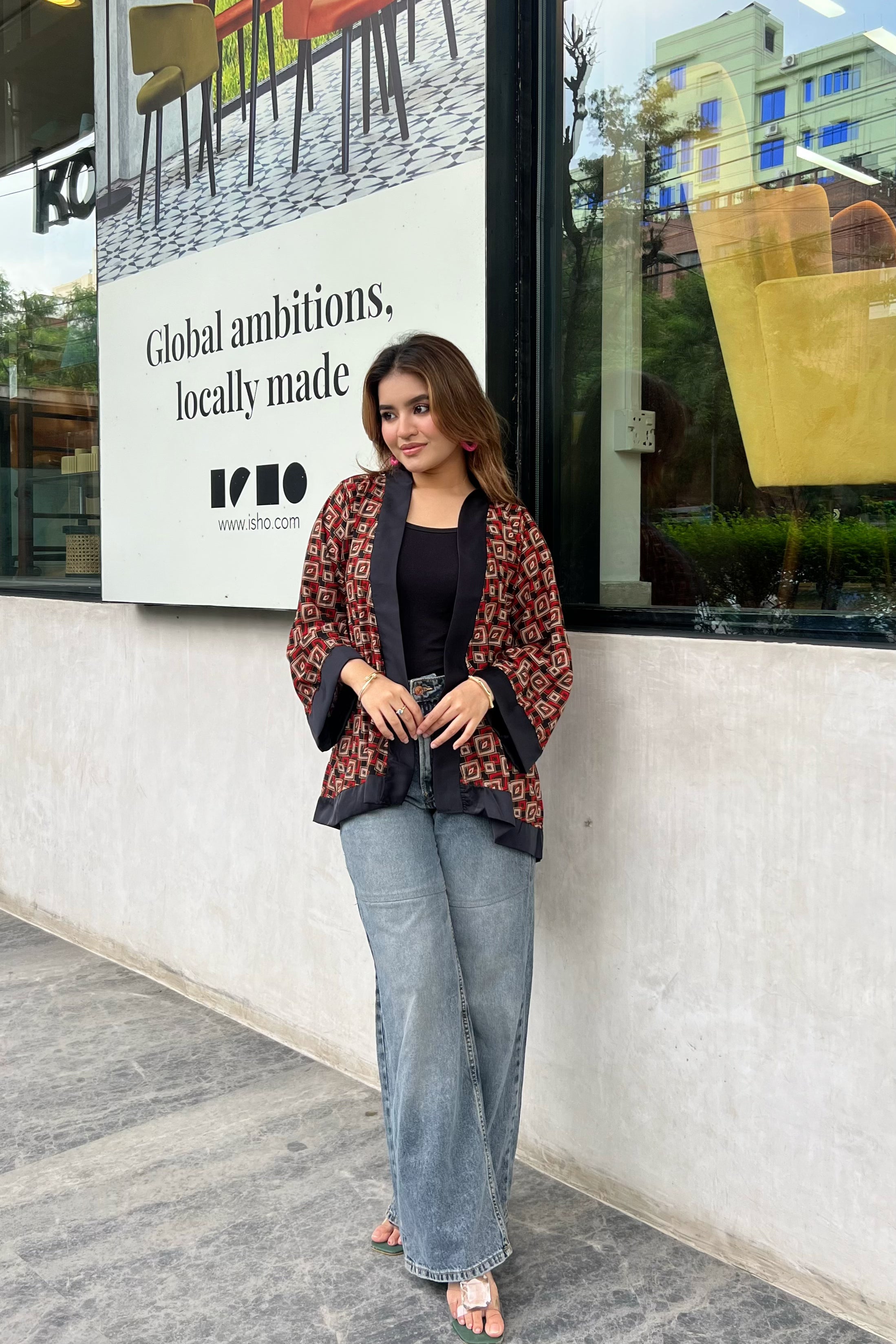 Woman wearing short kimonos standing in front of a store window with an advertisement in the background