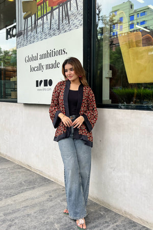 Woman wearing short kimonos standing in front of a store window with an advertisement in the background