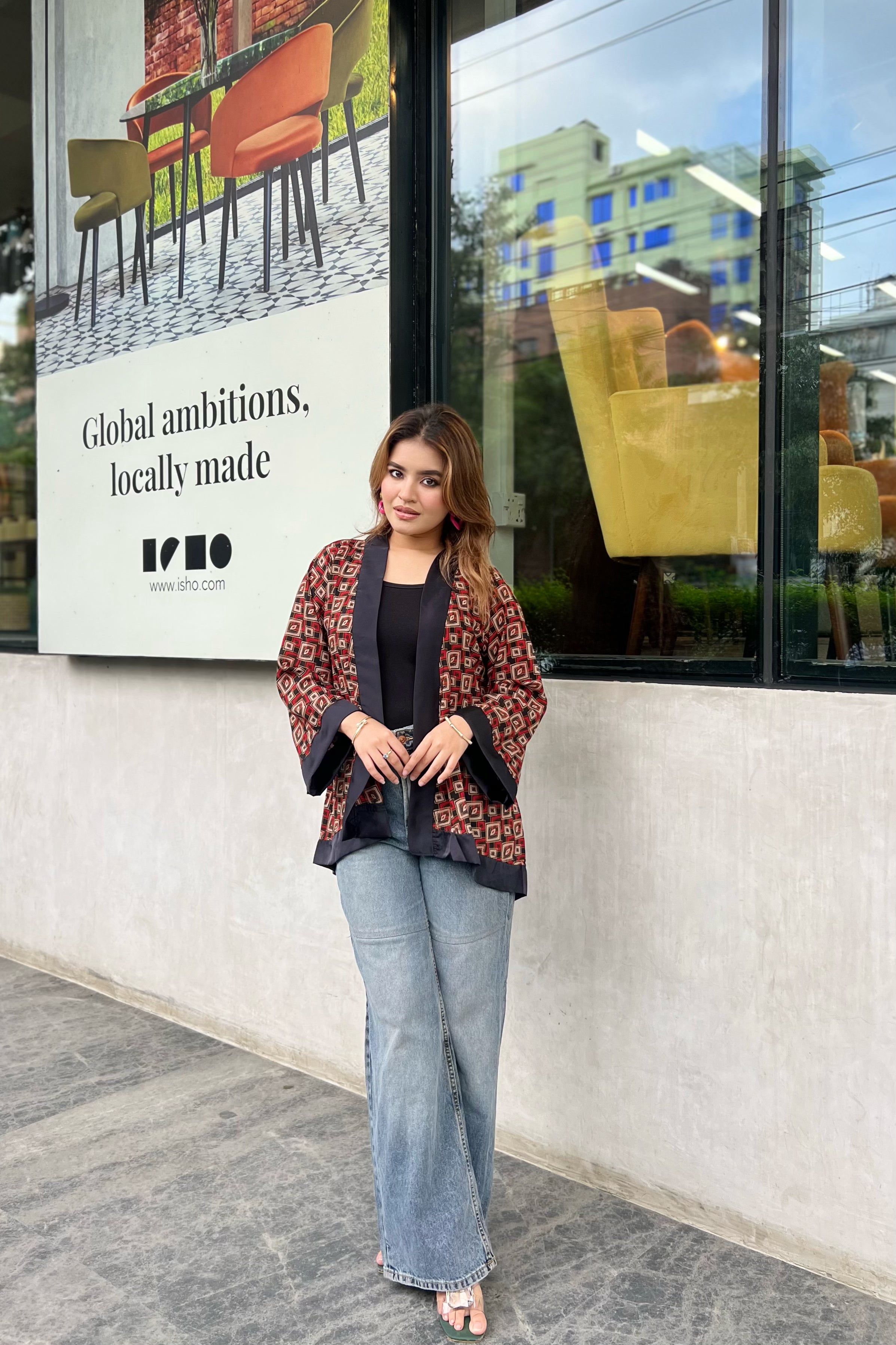 Woman wearing short kimonos standing in front of a building with a large sign and chairs displayed.