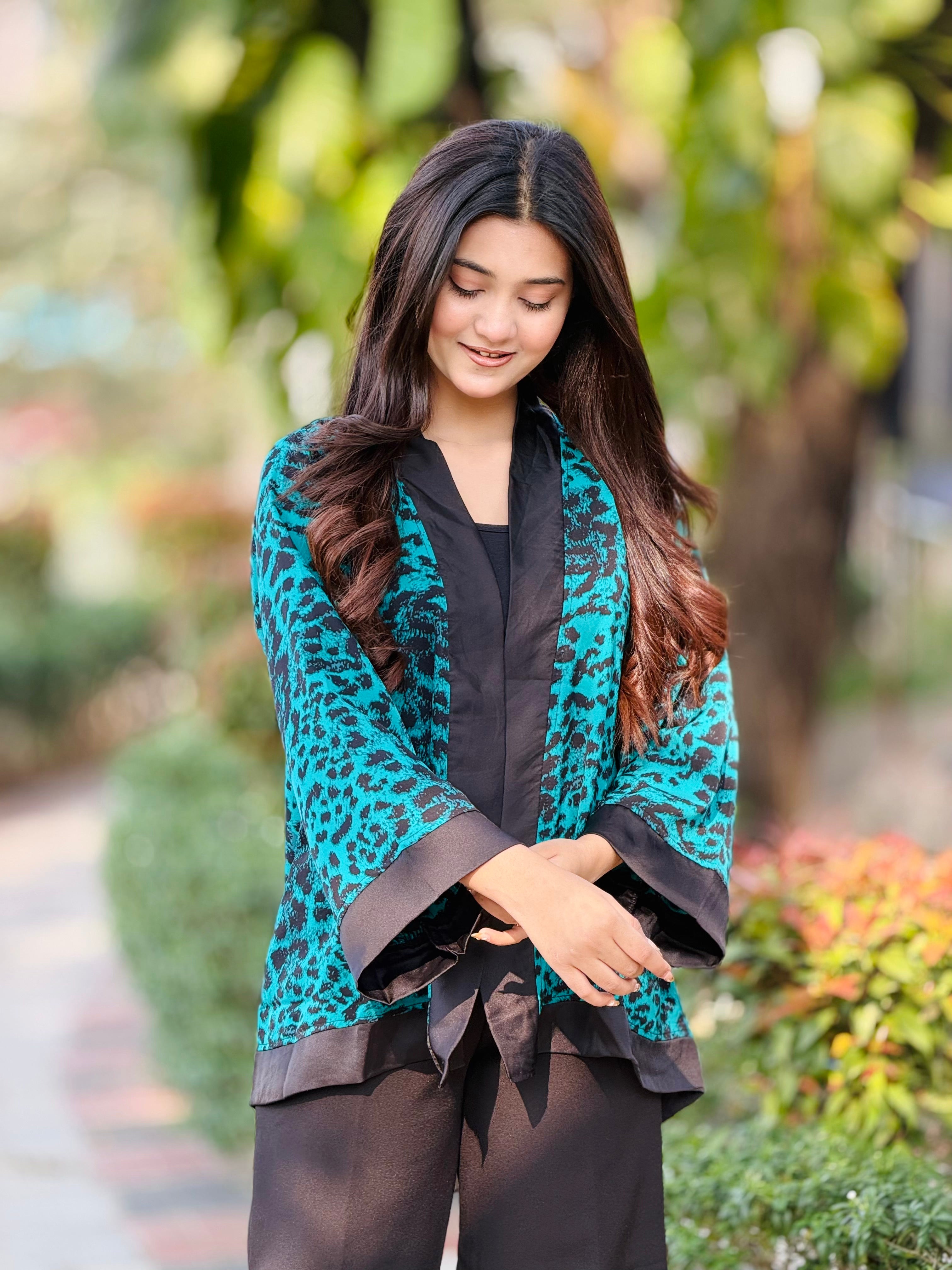 Woman wearing a teal leopard print kimono-style top with black trim outdoors.