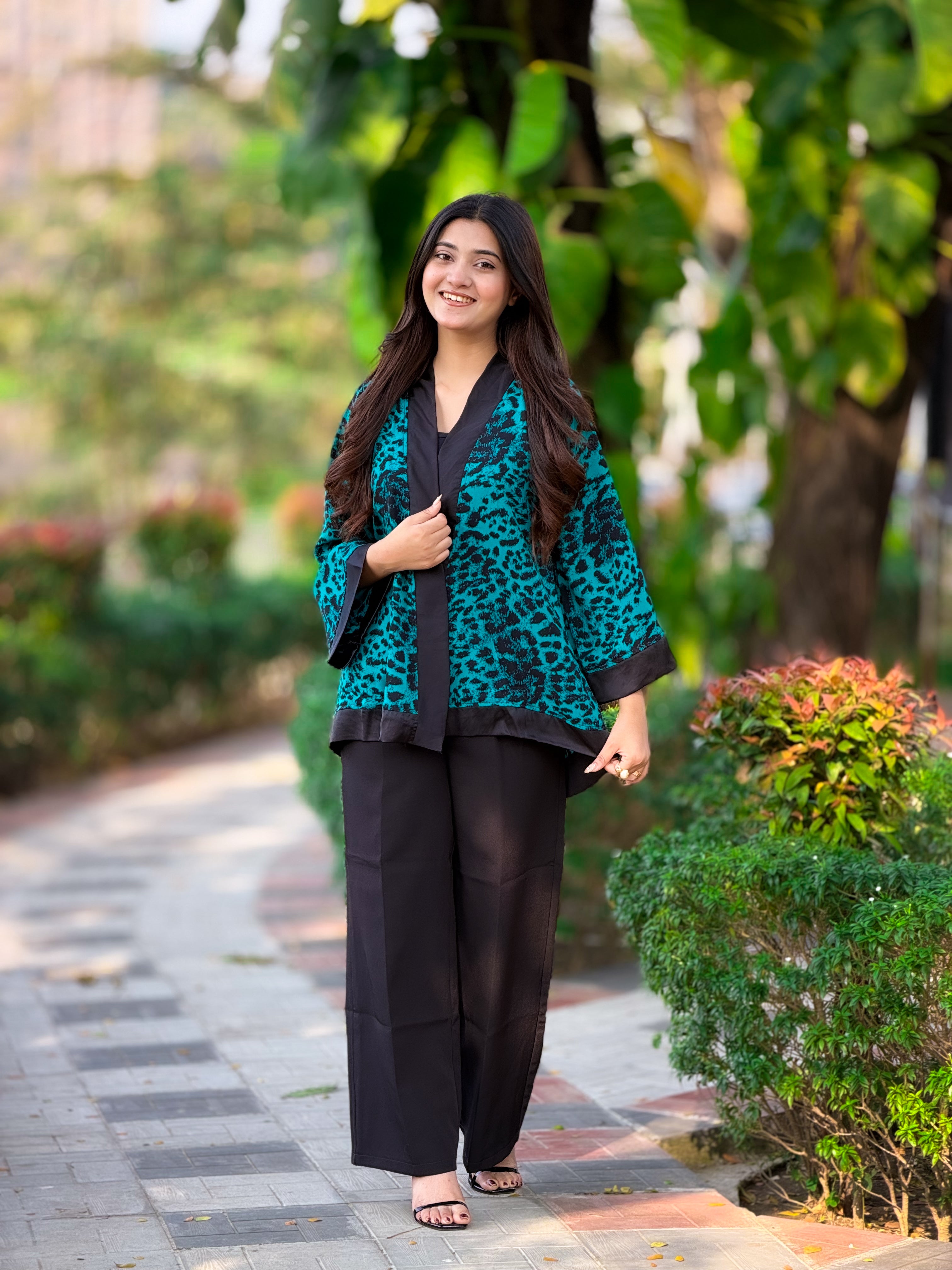 Woman in a teal and black outfit standing outdoors with greenery in the background