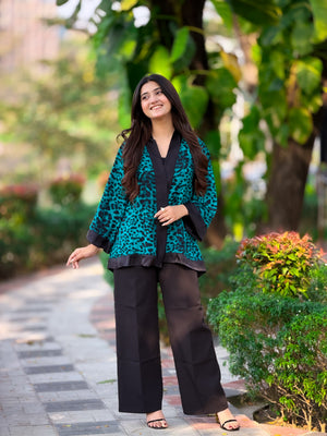 Woman in a teal and black outfit standing outdoors with greenery in the background