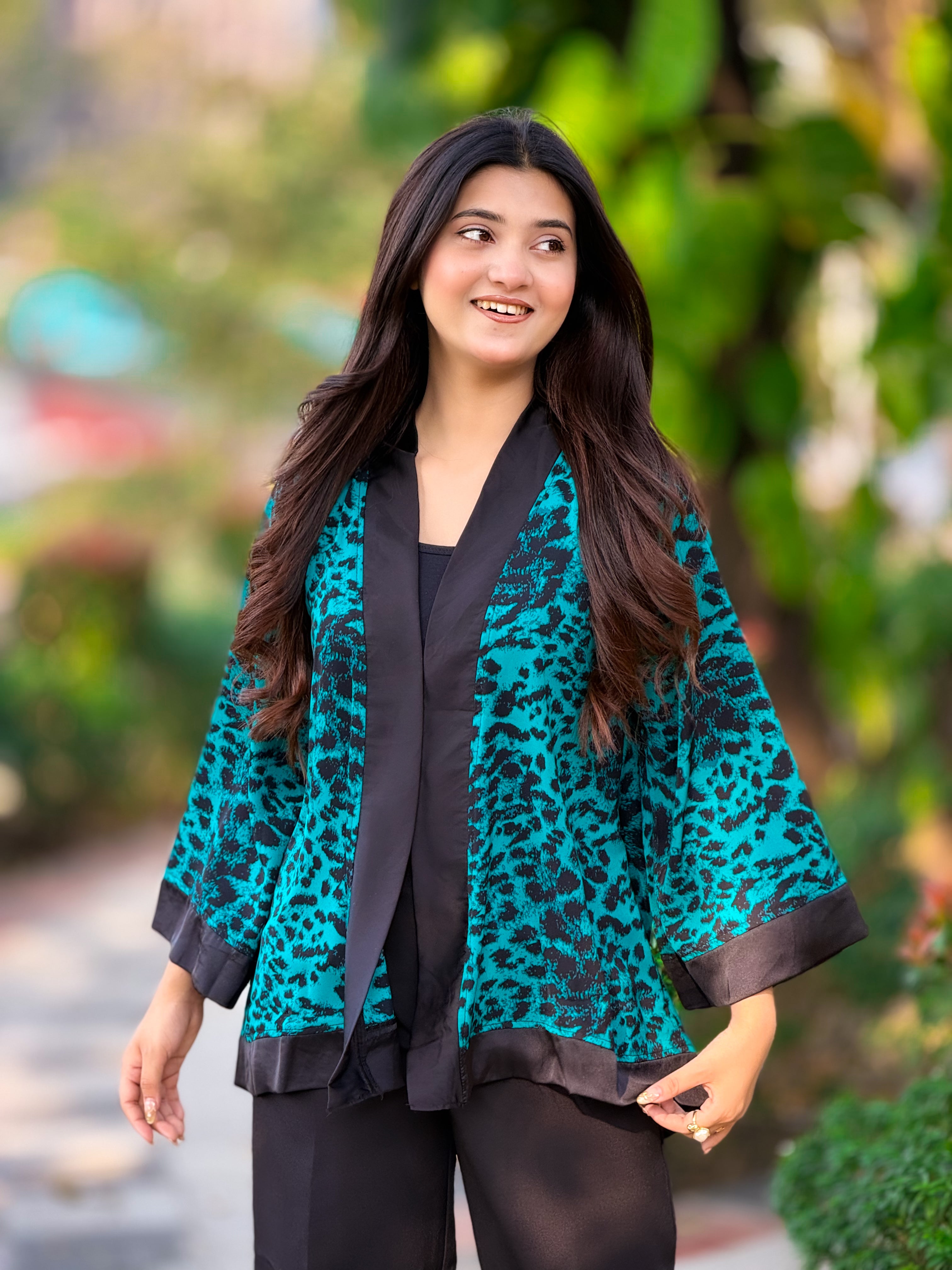 Woman wearing a teal leopard print kimono with a blurred green outdoor background