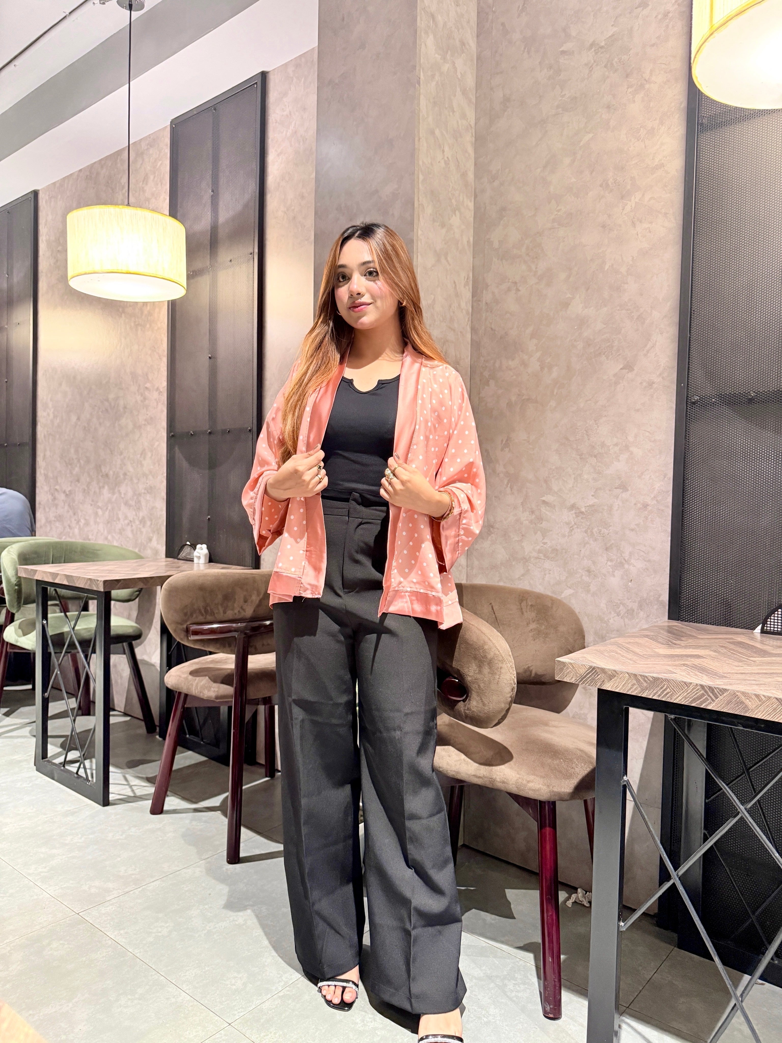 Woman standing in a modern cafe with tables and chairs wearing our Misty polka dot Kimono over a black top.