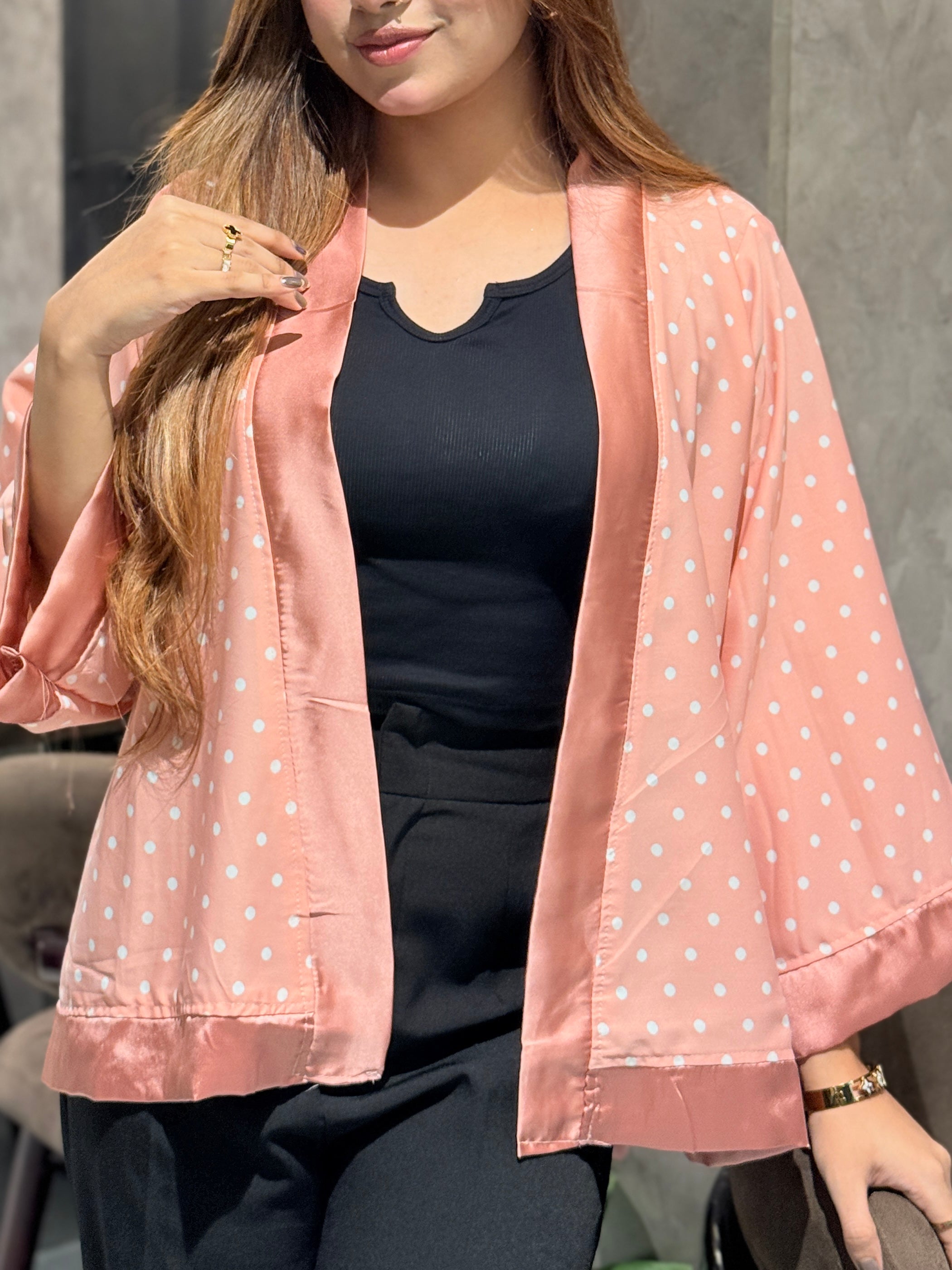 Woman wearing a pink polka dot kimono over a black top against a neutral background