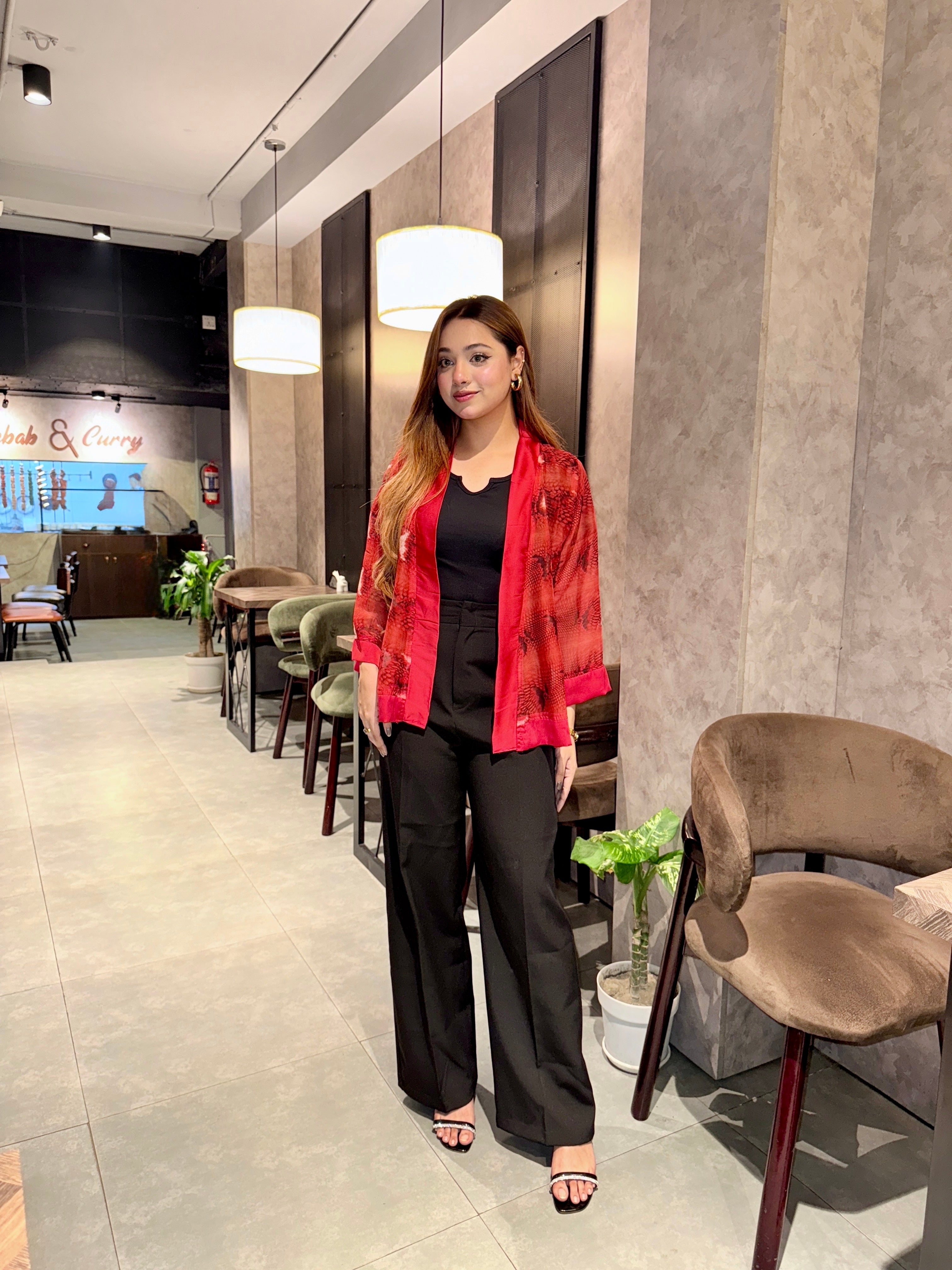 Woman in a red snake print kimono and black pants standing in a modern interior setting.