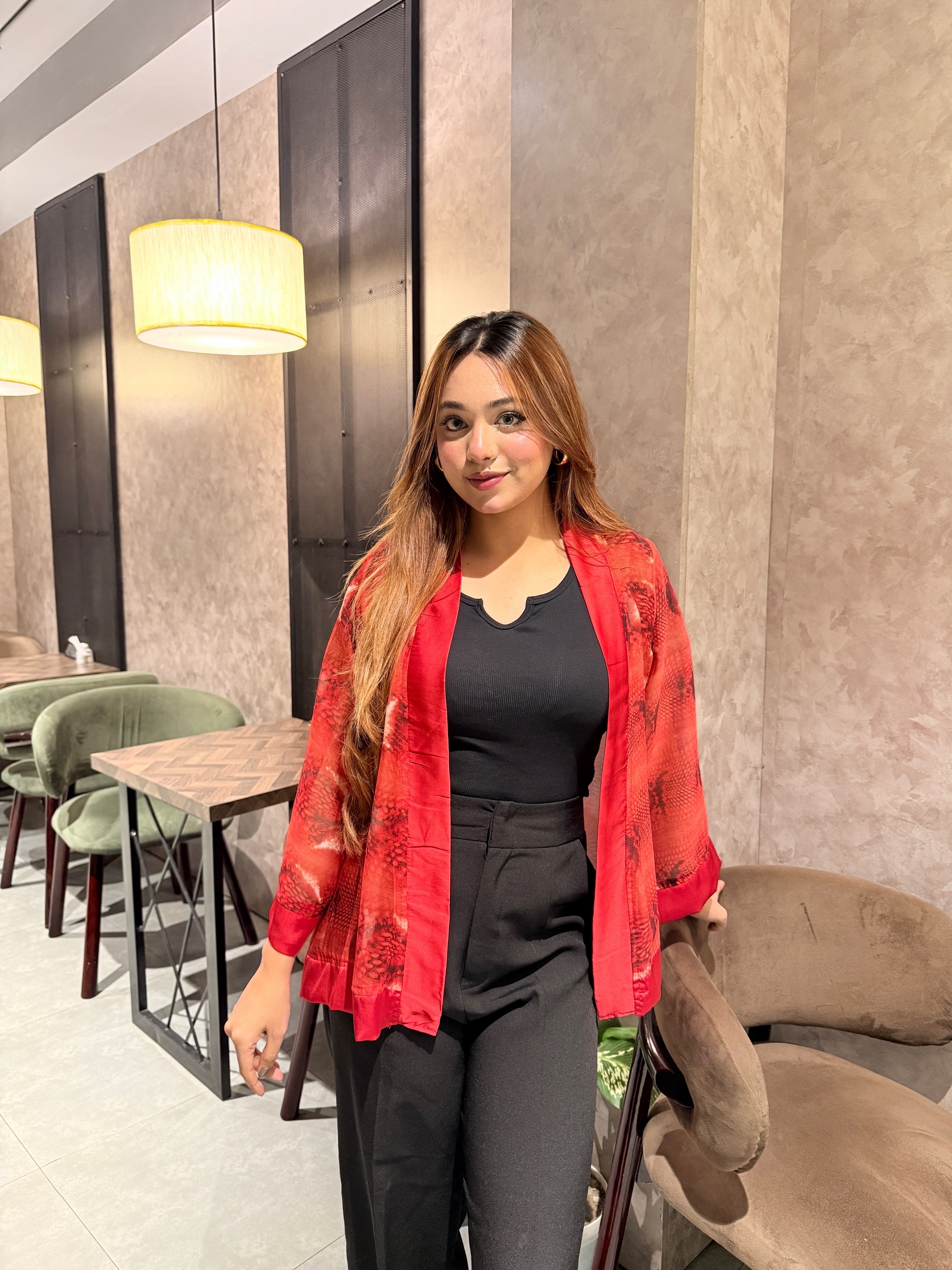 Woman wearing a red snake print kimono over a black top in a modern indoor setting