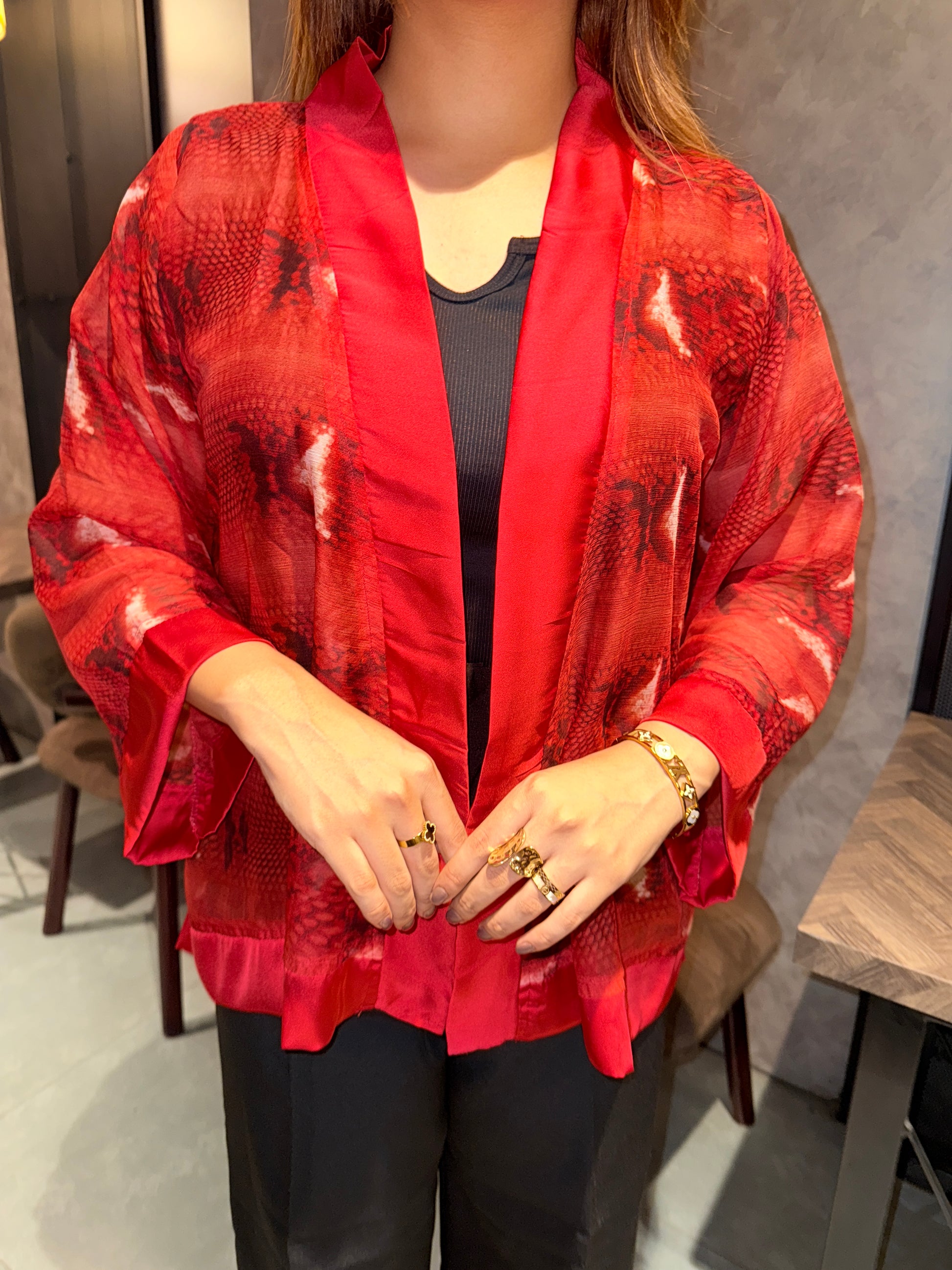 Person wearing ared snake print kimono with gold jewelry on a wooden floor.