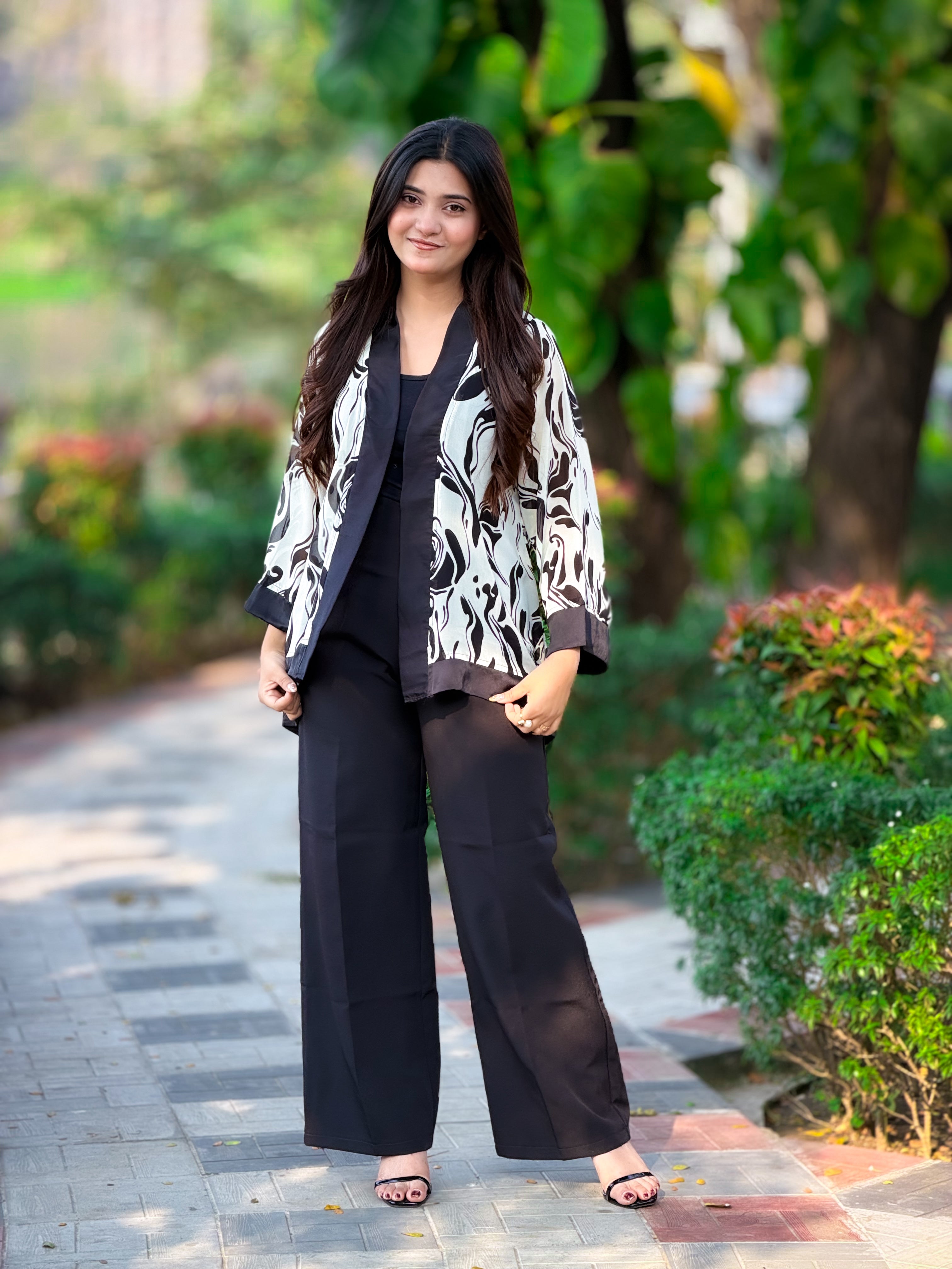 Woman in a stylish outfit standing outdoors with greenery in the background