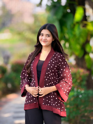Woman wearing a maroon polka dot jacket outdoors with greenery in the background