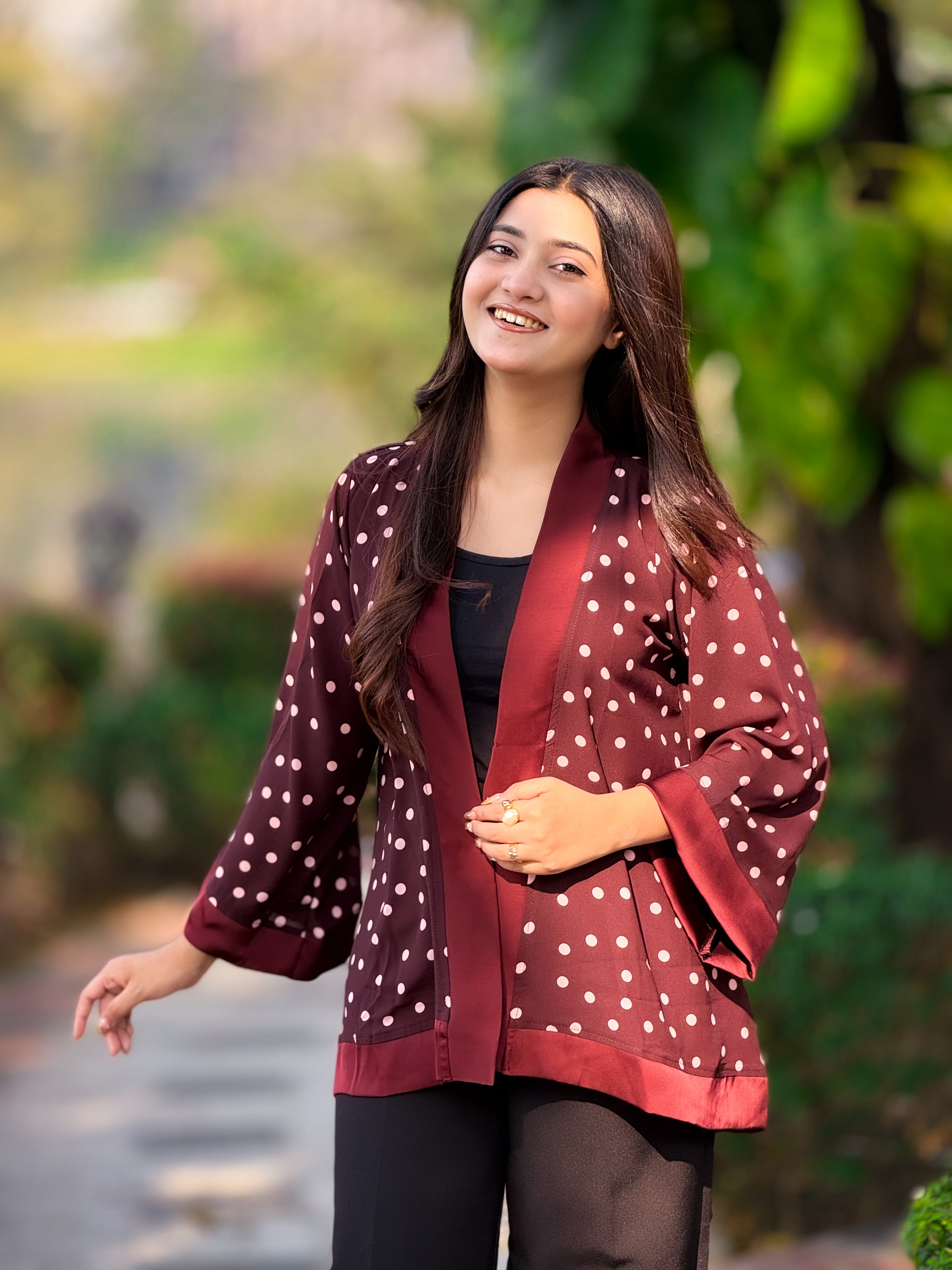 Woman wearing a polka dot jacket outdoors with greenery in the background