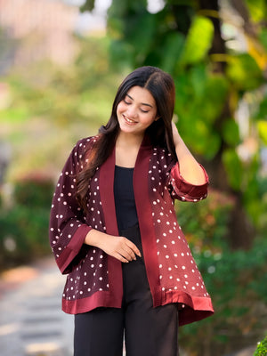 Woman wearing a maroon polka dot jacket outdoors with greenery in the background