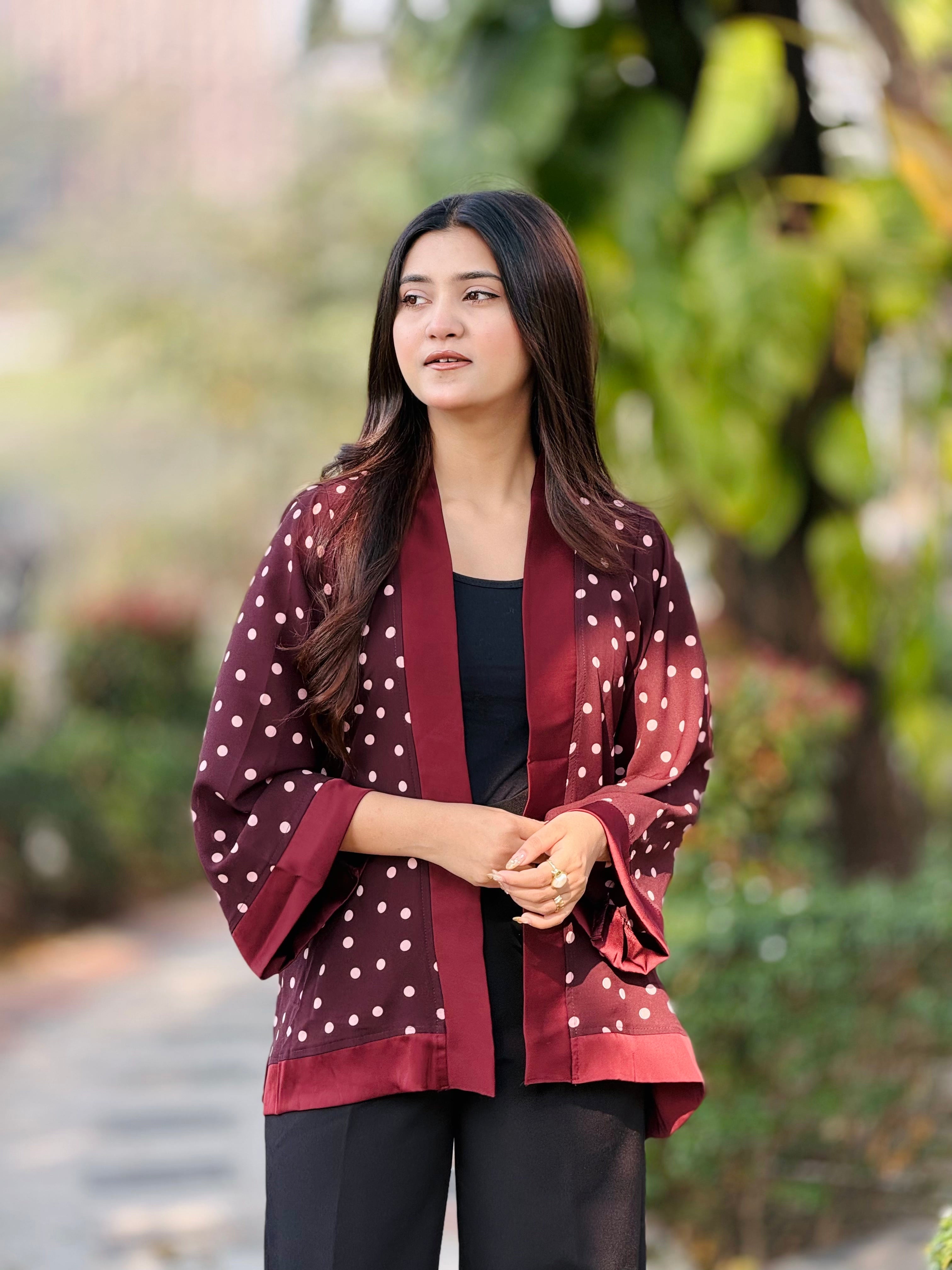 Woman wearing a maroon polka dot kimono-style jacket outdoors with greenery in the background