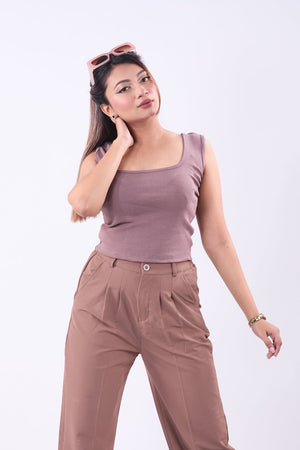 Woman wearing a mauve tank top and brown pants on a white background