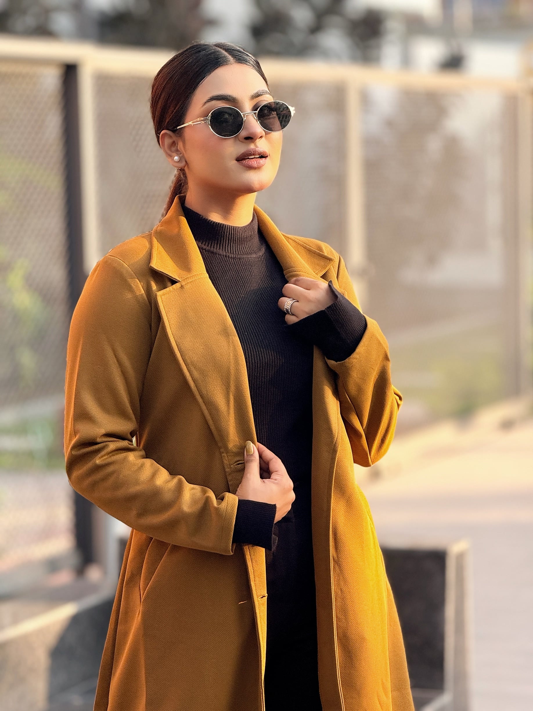 Woman wearing a mustard yellow coat and sunglasses outdoors.