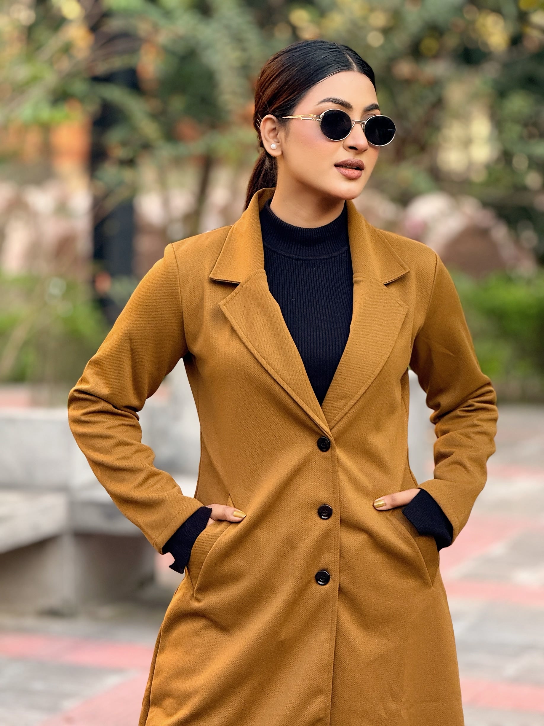 Woman wearing a mustard yellow coat and sunglasses outdoors.