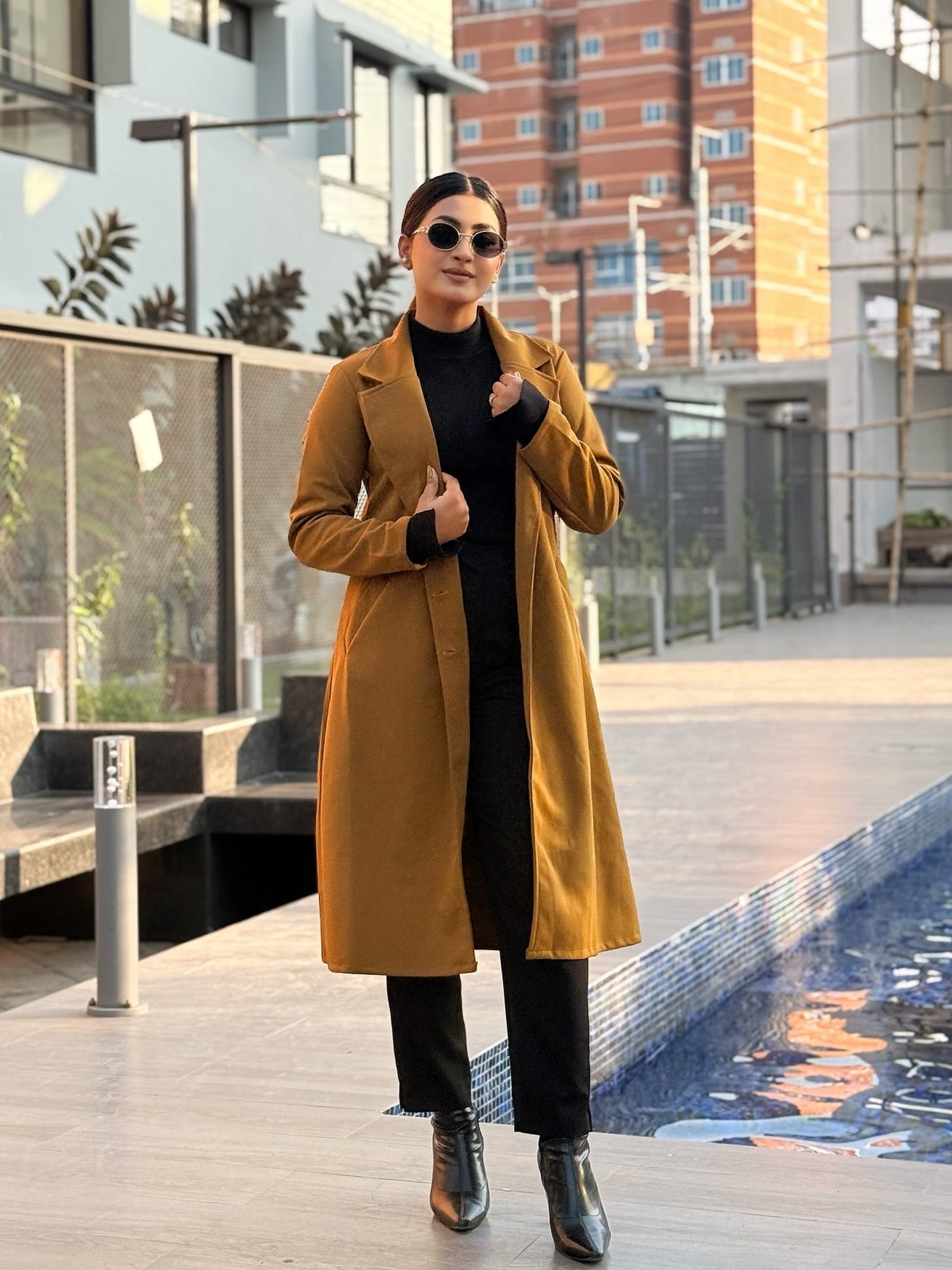 Person wearing a yellow coat standing by a pool with buildings in the background