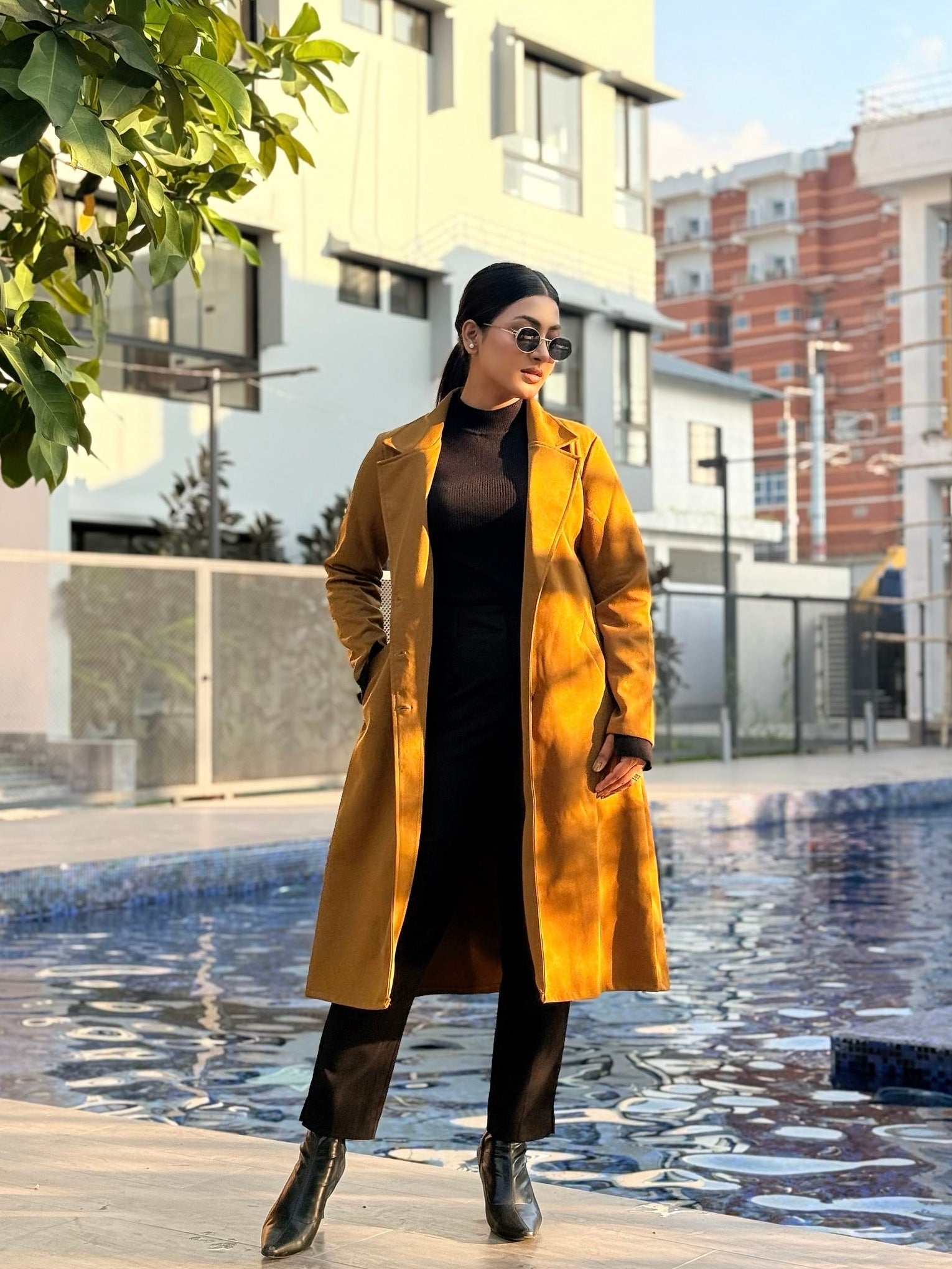 Woman in a yellow coat standing by a pool with buildings in the background