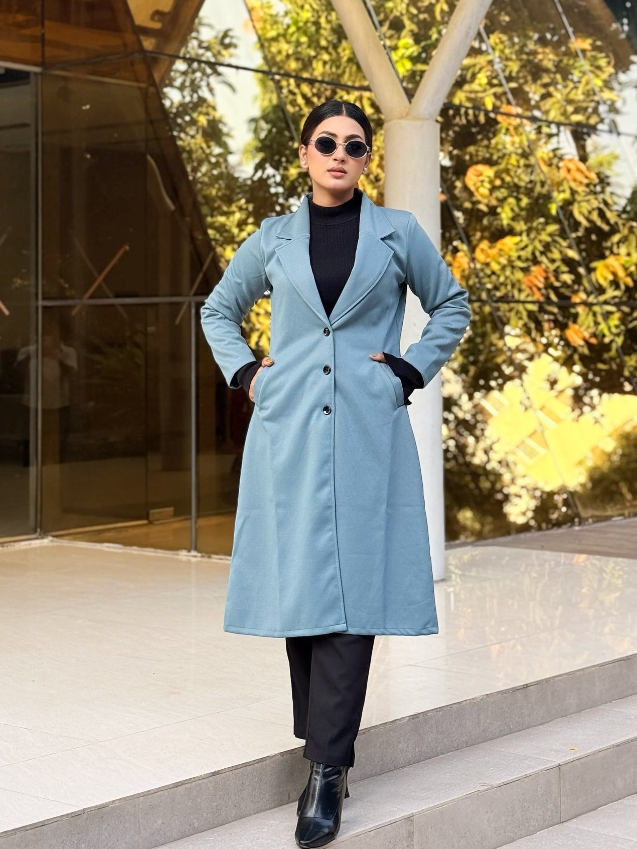 Person wearing a light blue coat standing on steps with a modern building and trees in the background