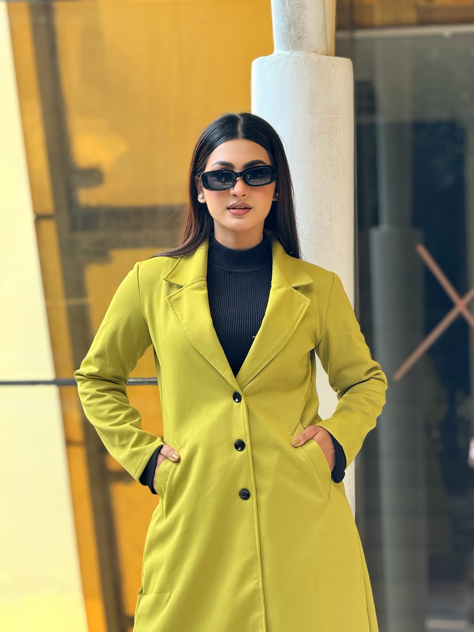 Woman wearing a bright yellow coat and sunglasses in an urban setting
