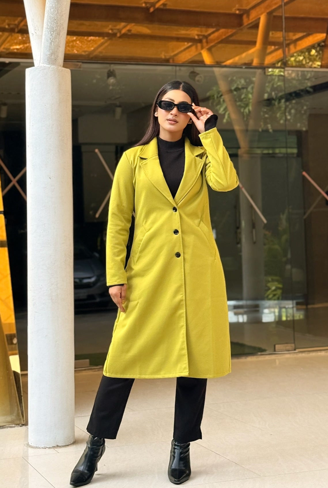 Person wearing a bright yellow coat standing in front of a modern building entrance.