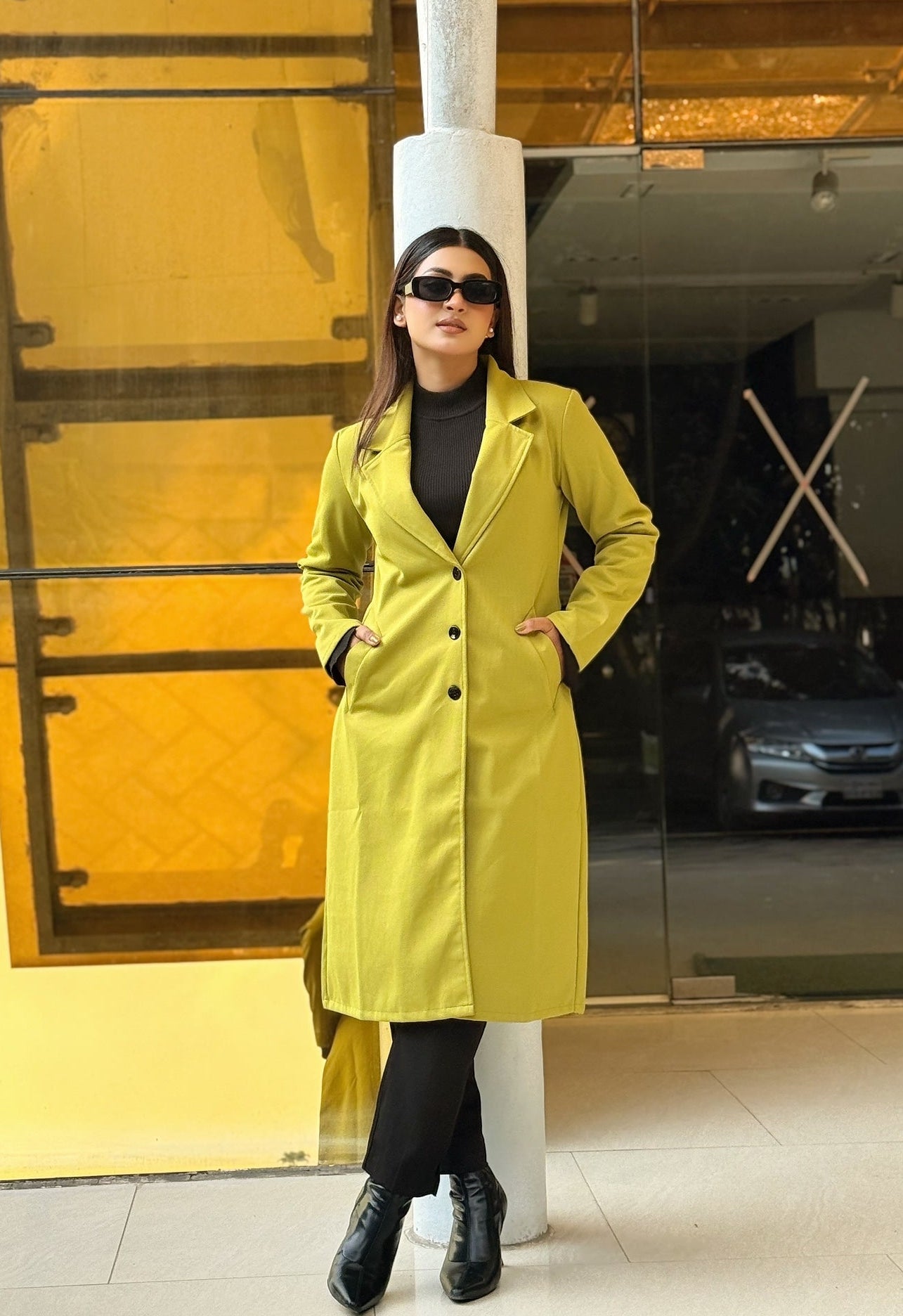 Person wearing a bright yellow coat standing in front of a glass wall.