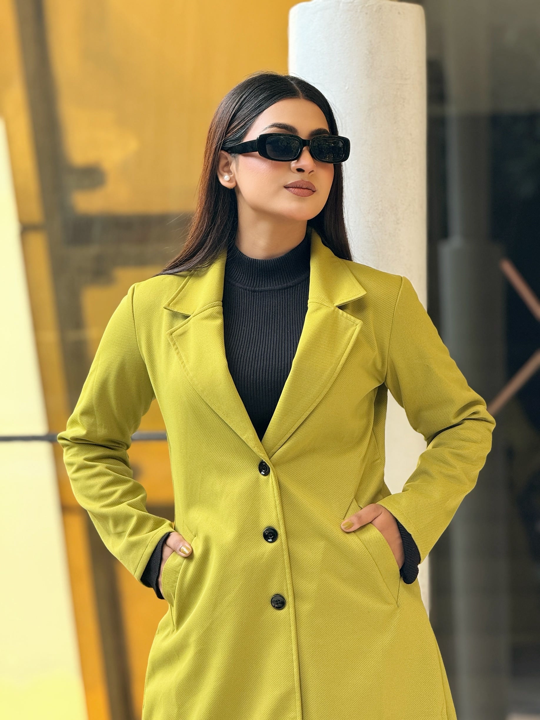 Woman wearing a yellow coat and sunglasses in an urban setting